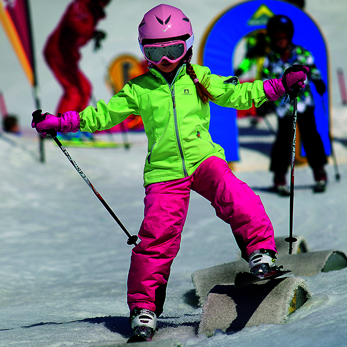 Kinderskilauf Geländeform Kind in pink-grünem Ski-Anzug und Skiern über Hindernissen